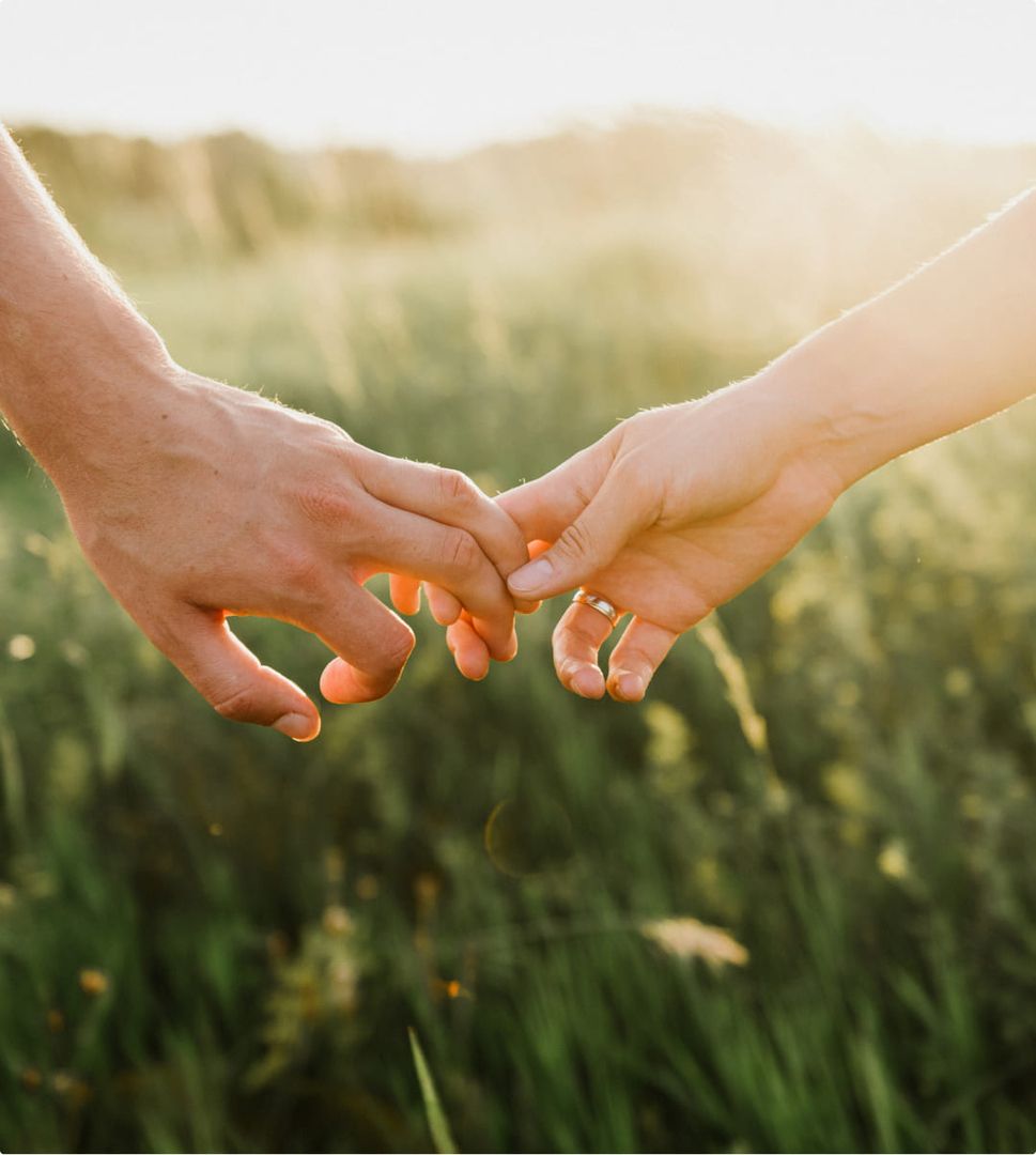 Hände halten sich im Sonnenschein auf einem grünen Feld