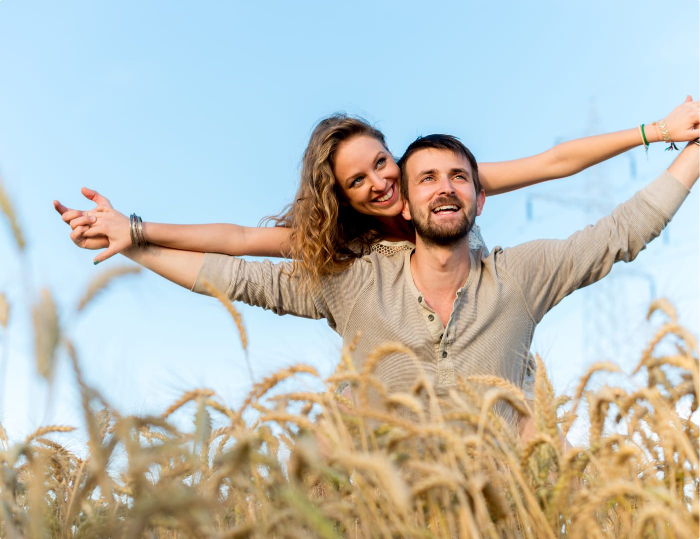 Lachende, blonde Frau wird auf dem Rücken eines Mannes durch ein Feld getragen